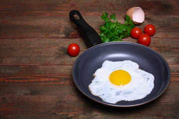 Pan of fried eggs, with cherry-tomatoes and parsley on a wooden table surface