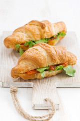 fresh croissant stuffed with fish and arugula on wooden board