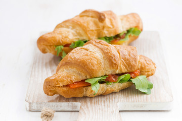 fresh croissant stuffed with fish and arugula on wooden board