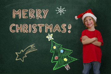 Little boy with Santa hat standing in front of a green blackboar