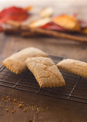 tre biscotti caserecci in primo piano su griglia, foglie autunnali e cannella in sfondo