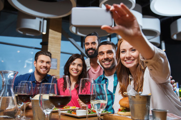 friends taking selfie by smartphone at restaurant