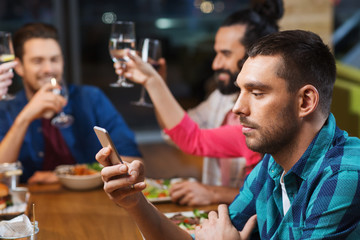 man with smartphone and friends at restaurant