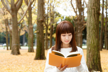 Obraz premium 紅葉した森で読書をする女性