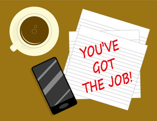 The message You Have Got The Job in red text written on notepaper next to a cup of coffee and a smartphone seen from overhead
