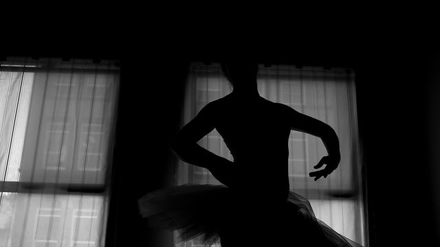 Black and white silhouette of a ballerina dancing in front of a window