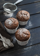 Delicious vegan chocolate muffins with icing sugar on dark wooden surface