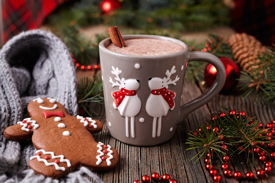 Cup of hot chocolate or cocoa with two cute deer, cinnamon and gingerbread man cookie in new year tree decorations frame on vintage wooden table background. Homemade traditional celebration recipe