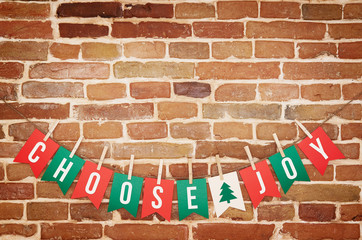 Red, green and white CHOOSE JOY and twig tree paper card DIY flag garland decoration on rustic brick wall background postcard.