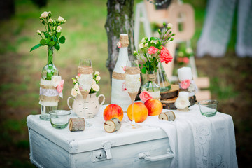 Wedding decor with bottles, glasses, roses, vases and peaches on a ancient suitcase. Decoration of a wedding photoshoot.  Details of a wedding decor.