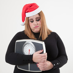 Worried woman with Santa hat holding a scale