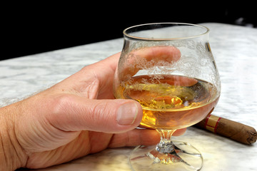 Hand of a man with a cigar and a glass of brandy