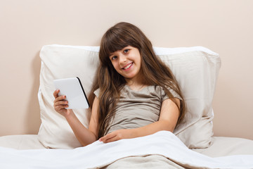 Little girl using digital tablet in bed 