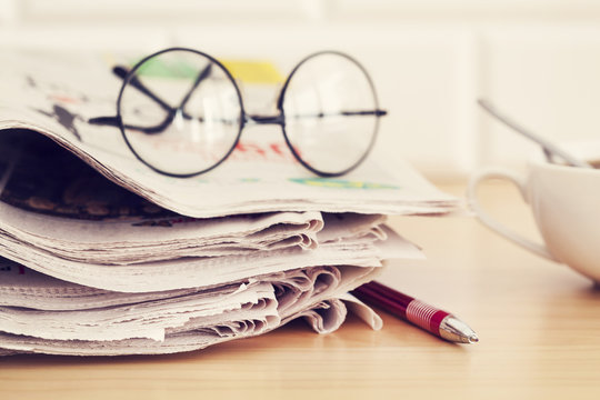Stack of newspapers, eyeglasses on table