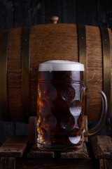 Huge beer mug on old wooden crate with vintage beer barrel on background, dark still life