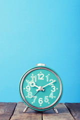 Blue retro clock on wooden table, vertical still life with copy space, vintage toned