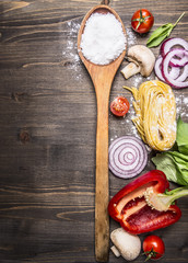 raw pasta with mushrooms, peppers, basil and chives and vintage wooden spoon on wooden rustic background top view close up border, place for text 