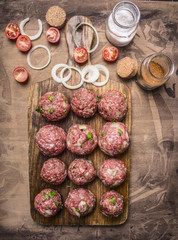 balls of minced meat on a cutting board with cherry tomatoes and seasonings on wooden rustic background top view close up