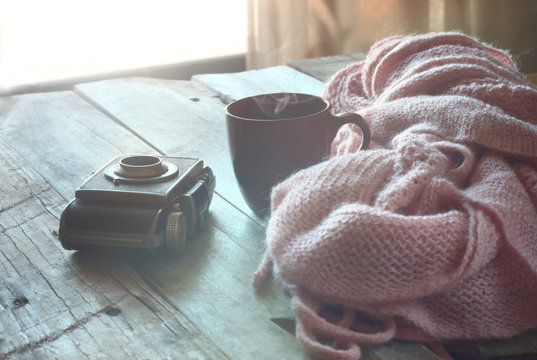 selective focus photo of pink cozy knitted scarf with to cup of coffee next to old photo camera on a wooden table. faded style retro filtered
