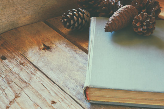 old book next to pine cones on wooden table. retro filtered. selective focus