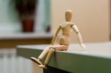 Wooden mannequin or man figurine sitting on white surface. 