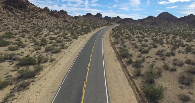 A moving aerial video clip shot at 4K in a desert road and ends passing through some rocky hills.