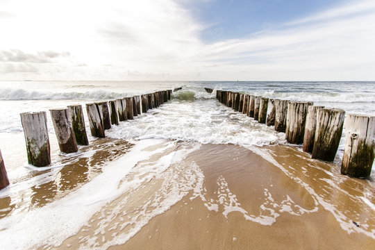 Wellenbrecher Pf&auml;hle an der Niederl&auml;ndischen Nordseek&uuml;ste in der Brandung bei tiefstehender Sonne vor malerischer Meereskulisse