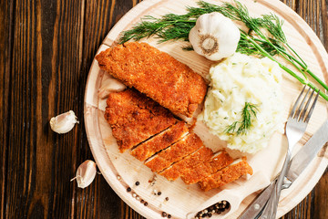 
meat with garnish , chicken cutlets in breadcrumbs , boiled mashed potatoes with herbs , garlic and spices on a wooden background