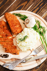 
meat with garnish , chicken cutlets in breadcrumbs , boiled mashed potatoes with herbs , garlic and spices on a wooden background