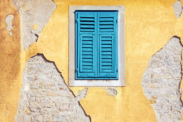 Peeling paint on a yellow house façade with a blue window.