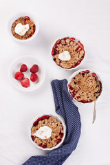 Crumble with oatmeal, wholemeal and strawberry in white bowls on a white table.