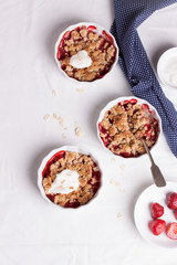 Crumble with oatmeal, wholemeal and strawberry in white bowls on a white table. Top view.