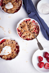 Crumble with oatmeal, wholemeal and strawberry in white bowls on a white table. Top view.