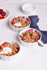 Crumble with oatmeal, wholemeal and strawberry in white bowls on a white table.