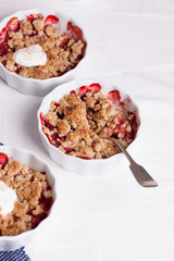 Crumble with oatmeal, wholemeal and strawberry in white bowls on a white table