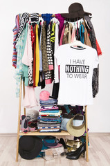 Many clothes on the rack with a t-shirt saying nothing to wear. Close up on a cluttered wardrobe with colorful clothes and accessories, many clothes and nothing to wear.