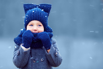 cute little boy, kid in winter clothes walking under the snow