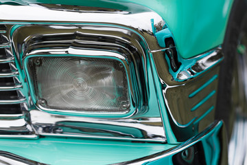 Close-up of rectangle shape headlight of a turquoise shiny classic vintage car