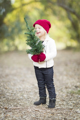 Baby Girl In Red Mittens and Cap Holding Small Christmas Tree