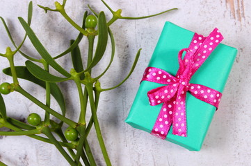 Wrapped green gift for Christmas and mistletoe on old wooden background
