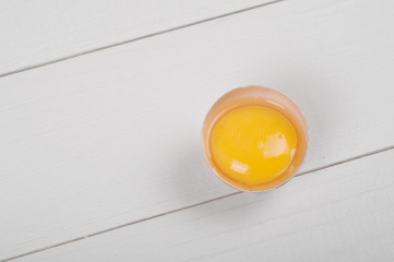 Broken raw brown egg on white wooden table