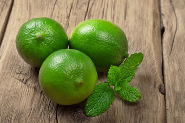Fresh limes with mint leaves on wooden surface