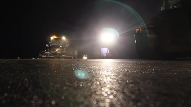 Road rollers leveling fresh asphalt pavement by night