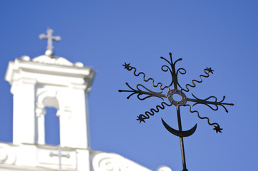 Closeup of black metal cross with a white church in the background