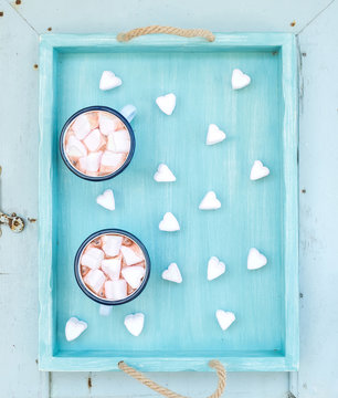 Seint Valentine's holiday greeting set. Hot chocolate and heart shaped marshmallows in old enamel mugs on turquoise serving tray over blue wooden background