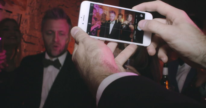 Hands of man taking smartphone photos of his friends dancing at a party