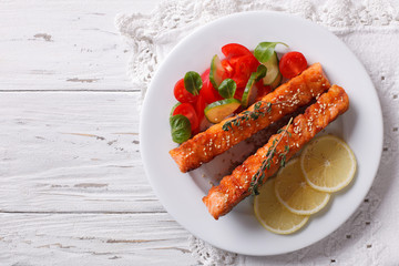 Grilled salmon with lemon and fresh salad on a plate. Horizontal top view
