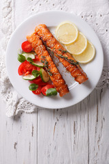 Grilled salmon with lemon and fresh salad on a plate. vertical top view
