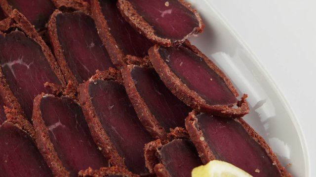 Basturma, pork dried meat with lemon on white plate