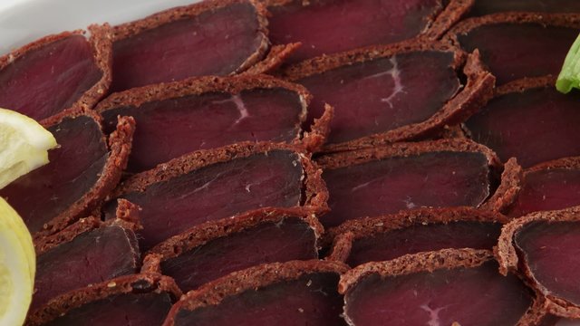 Basturma, pork dried meat with lemon on white plate